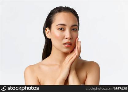 Skincare, bodycare, beauty and bath concept. Sensual beautiful asian woman standing naked, touching face gently and looking dreamy camera, apply facial cream, nourishing mask.. Skincare, bodycare, beauty and bath concept. Sensual beautiful asian woman standing naked, touching face gently and looking dreamy camera, apply facial cream, nourishing mask