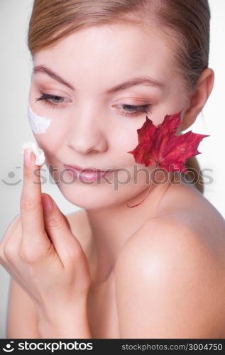 Skincare habits. Face of young woman with leaf as symbol of red capillary skin on gray. Girl taking care of her dry complexion applying moisturizing cream. Beauty treatment.