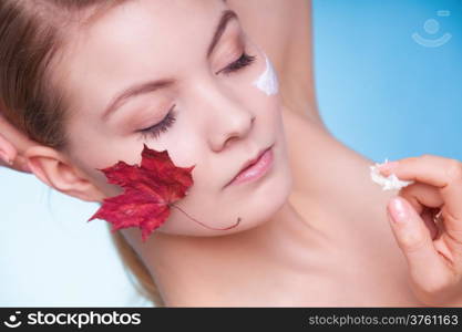 Skincare habits. Face of young woman with leaf as symbol of red capillary skin on blue. Girl taking care of her dry complexion applying moisturizing cream. Beauty treatment.