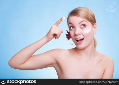 Skincare habits. Face of young woman with leaf as symbol of red capillary skin on blue. Girl taking care of her dry complexion applying moisturizing cream. Beauty treatment.