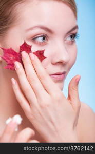 Skincare habits. Face of young woman with leaf as symbol of red capillary skin on blue. Girl taking care of her dry complexion applying moisturizing cream. Beauty treatment.