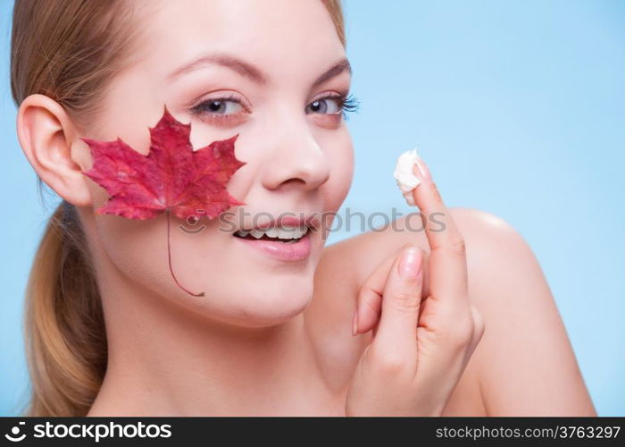 Skincare habits. Face of young woman with leaf as symbol of red capillary skin on blue. Girl taking care of her dry complexion applying moisturizing cream. Beauty treatment.