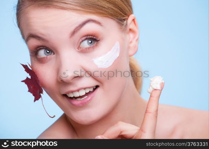 Skincare habits. Face of young woman with leaf as symbol of red capillary skin on blue. Girl taking care of her dry complexion applying moisturizing cream. Beauty treatment.