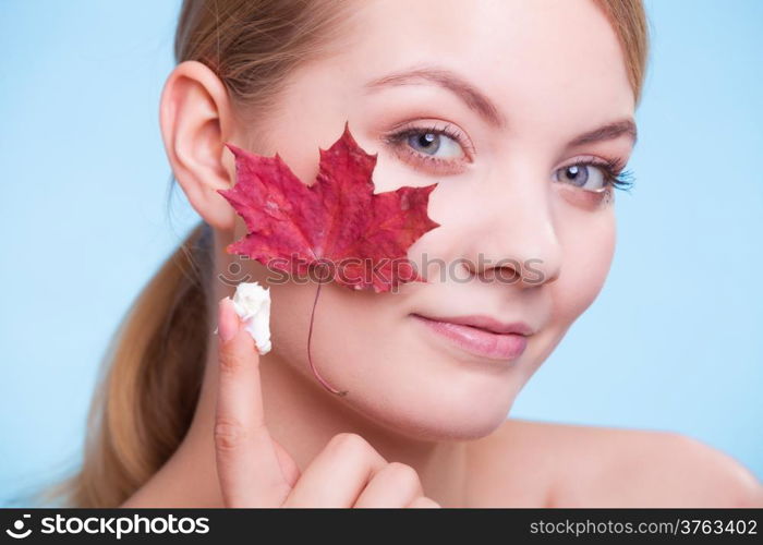 Skincare habits. Face of young woman with leaf as symbol of red capillary skin on blue. Girl taking care of her dry complexion applying moisturizing cream. Beauty treatment.