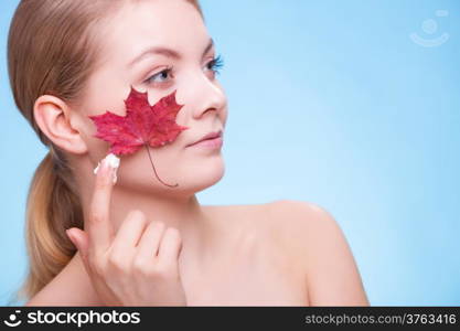 Skincare habits. Face of young woman with leaf as symbol of red capillary skin on blue. Girl taking care of her dry complexion applying moisturizing cream. Beauty treatment.