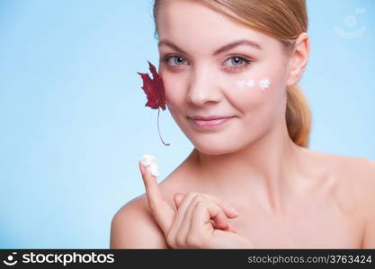 Skincare habits. Face of young woman with leaf as symbol of red capillary skin on blue. Girl taking care of her dry complexion applying moisturizing cream. Beauty treatment.