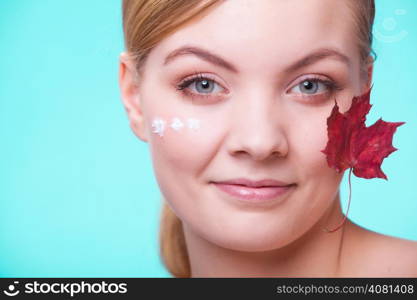 Skincare habits. Face of young woman with leaf as symbol of red capillary skin on turquoise. Girl taking care of her dry complexion applying moisturizing cream. Beauty treatment.