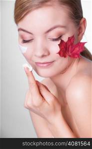 Skincare habits. Face of young woman with leaf as symbol of red capillary skin on gray. Girl taking care of her dry complexion applying moisturizing cream. Beauty treatment.