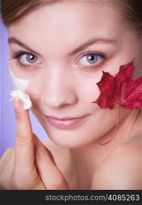 Skincare habits. Face of young woman with leaf as symbol of red capillary skin on gray. Girl taking care of her dry complexion applying moisturizing cream. Beauty treatment.