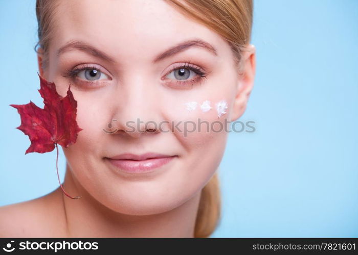 Skincare habits. Face of young woman with leaf as symbol of red capillary skin on blue. Girl taking care of her dry complexion applying moisturizing cream. Beauty treatment.