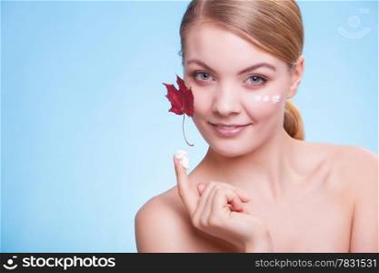 Skincare habits. Face of young woman with leaf as symbol of red capillary skin on blue. Girl taking care of her dry complexion applying moisturizing cream. Beauty treatment.