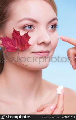 Skincare habits. Face of young woman with leaf as symbol of red capillary skin on blue. Girl taking care of her dry complexion applying moisturizing cream. Beauty treatment.