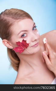 Skincare habits. Face of young woman with leaf as symbol of red capillary skin on blue. Girl taking care of her dry complexion applying moisturizing cream. Beauty treatment.