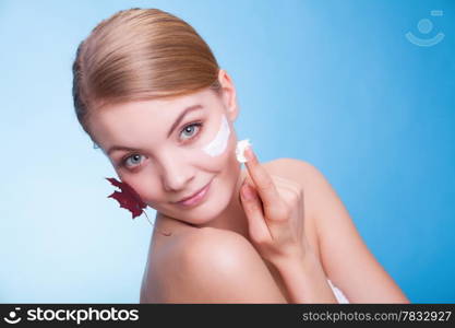 Skincare habits. Face of young woman with leaf as symbol of red capillary skin on blue. Girl taking care of her dry complexion applying moisturizing cream. Beauty treatment.