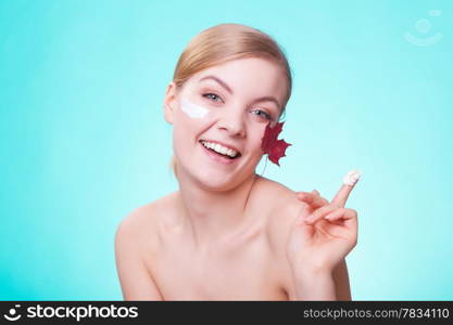 Skincare habits. Face of young woman with leaf as symbol of red capillary skin on turquoise. Girl taking care of her dry complexion applying moisturizing cream. Beauty treatment.