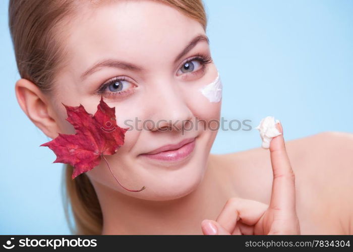 Skincare habits. Face of young woman with leaf as symbol of red capillary skin on blue. Girl taking care of her dry complexion applying moisturizing cream. Beauty treatment.