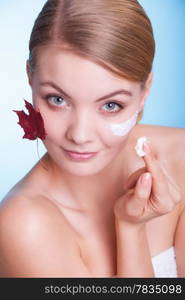 Skincare habits. Face of young woman with leaf as symbol of red capillary skin on blue. Girl taking care of her dry complexion applying moisturizing cream. Beauty treatment.