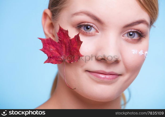 Skincare habits. Face of young woman with leaf as symbol of red capillary skin on blue. Girl taking care of her dry complexion applying moisturizing cream. Beauty treatment.