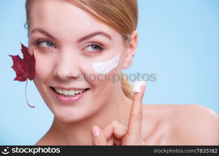 Skincare habits. Face of young woman with leaf as symbol of red capillary skin on blue. Girl taking care of her dry complexion applying moisturizing cream. Beauty treatment.