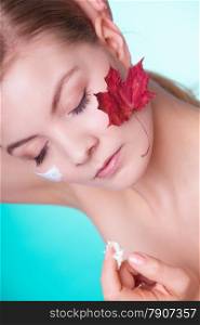 Skincare habits. Face of young woman with leaf as symbol of red capillary skin on turquoise. Girl taking care of her dry complexion applying moisturizing cream. Beauty treatment.