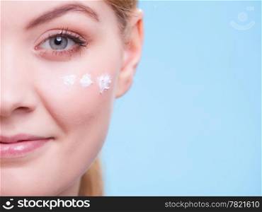 Skincare habits. Part of face of young woman as symbol of red capillary skin on blue. Girl taking care of her dry complexion applying moisturizing cream. Beauty treatment.