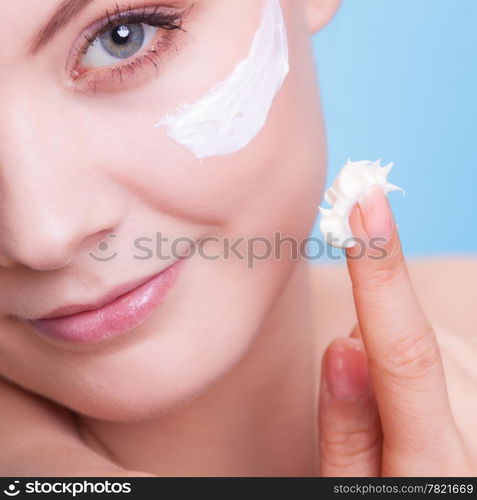 Skincare habits. Part of face of young woman as symbol of red capillary skin on blue. Girl taking care of her dry complexion applying moisturizing cream. Beauty treatment.