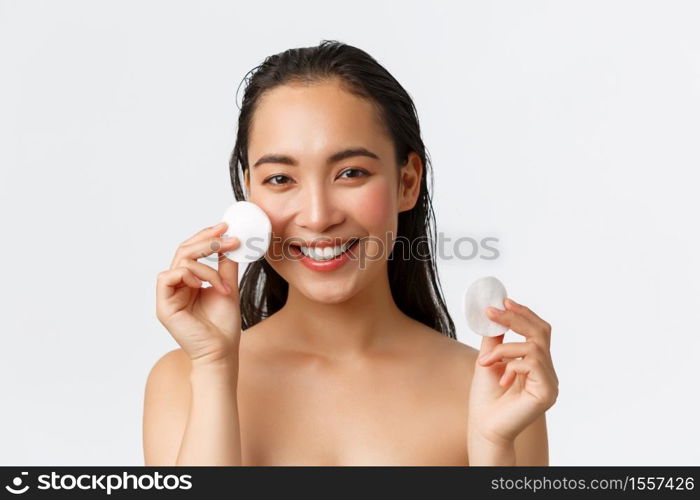 Skincare, women beauty, hygiene and personal care concept. Close-up of beautiful asian girl standing naked and showing cotton pads near face, wipe-off makeup before shower, white background.. Skincare, women beauty, hygiene and personal care concept. Close-up of beautiful asian girl standing naked and showing cotton pads near face, wipe-off makeup before shower, white background