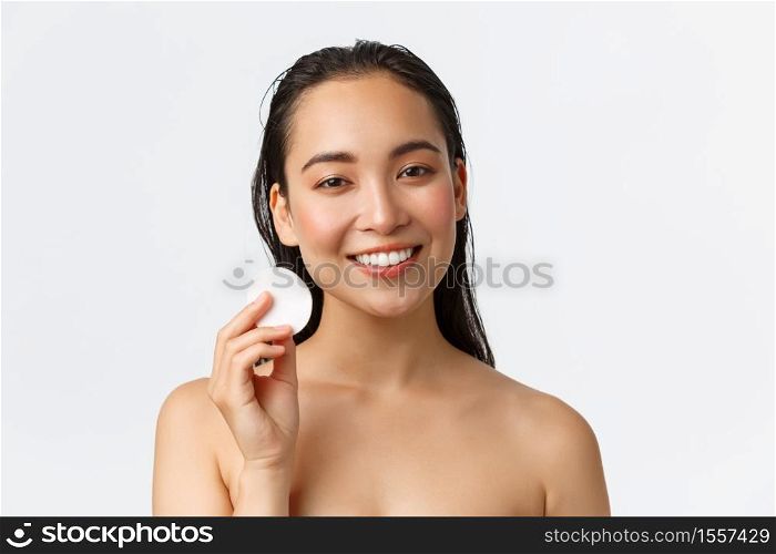 Skincare, women beauty, hygiene and personal care concept. Close-up of beautiful asian female standing naked and using cotton pad to apply cleanser on fresh clean skin, white background.. Skincare, women beauty, hygiene and personal care concept. Close-up of beautiful asian female standing naked and using cotton pad to apply cleanser on fresh clean skin, white background