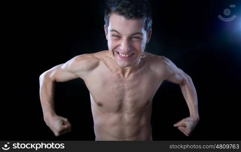 skinny young man making muscle against black background