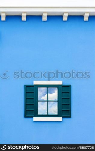 Sky and cloud reflection in green window glass on blue wall of house, Italy retro style