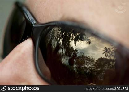 Sky and forest reflected in lenses of black sunglasses