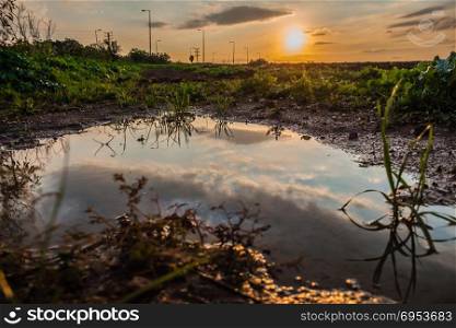 Sky reflected in a puddle of water in a field at sunset.