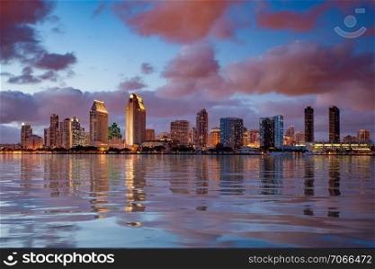 Skyline cityscape of San Diego downtown skyscrapers at night with lights reflecting into a digital ocean. San Diego skyline at dusk reflected in sea