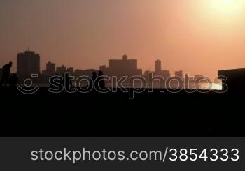 Skyline in La Habana, Cuba, at sunset, with vintage cars on the street and people sitting on the Malecon promenade, with ocean. Sequence