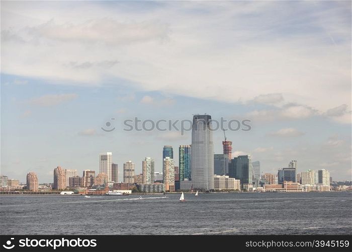skyline of jersey city with blue sky and white clouds seen from the water