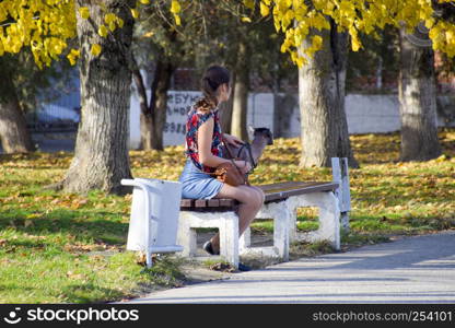 Slavyansk-on-Kuban, Russia - November 8, 2016: The lady with the dog in the park on the bench. Walking girl in the park. The dog is on a leash.. The lady with the dog in the park on the bench. Walking girl in the park. The dog is on a leash.
