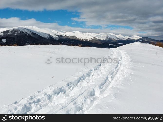 Sledge trace and footprints on winter mountain hill top and snow covered picturesque alp Chornohora ridge (Ukraine, Carpathian Mountains, tranquility peaceful view from Dzembronya village outskirts).. Sledge trace and footprints on winter mountain hill top