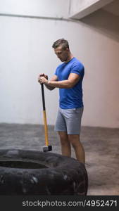 Sledgehammer Tire Hits young muscular man workout at gym with hammer and tractor tire