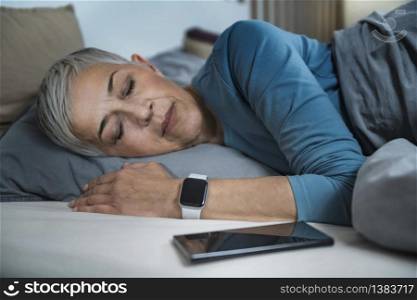 Sleep Apps - Tech-savvy Senior Woman Sleeping in Bed, Using Smart Phone and Smart Watch to Improve her Sleeping Habits