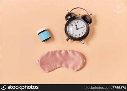 sleep disorder and bedtime concept - close up of alarm clock, eye sleeping mask and soporific medicine on beige background. alarm clock, eye sleeping mask and pills