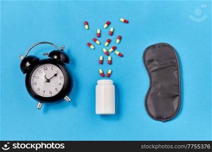 sleep disorder and bedtime concept - close up of alarm clock, eye sleeping mask and soporific medicine on blue background. alarm clock, eye sleeping mask and pills