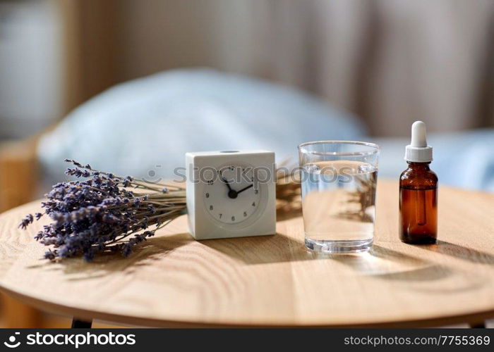 sleep disorder, bedtime and morning concept - close up of alarm clock, lavender essential oil and glass of water on night table at home. alarm clock, lavender oil and glass of water