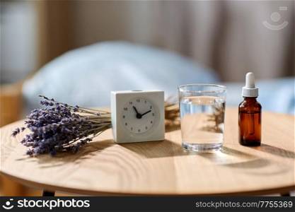 sleep disorder, bedtime and morning concept - close up of alarm clock, lavender essential oil and glass of water on night table at home. alarm clock, lavender oil and glass of water