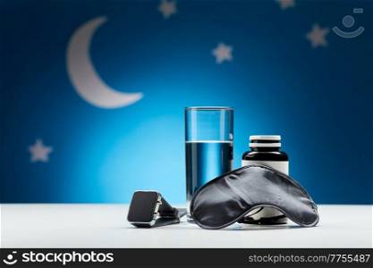 sleep disorder, bedtime and object concept - close up of smart watch, eye mask, glass of water and soporific medicine over moon and night stars on blue background. water, eye sleeping mask, smart watch and medicine