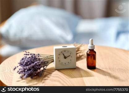 sleep disorder, bedtime, sleeping and morning concept - close up of alarm clock and lavender essential oil on night table at home. alarm clock and lavender essential oil on table