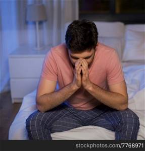sleep disorder, insomnia and mental health problems concept - unhappy man in pajamas sitting on bed at night. unhappy man in pajamas sitting on bed at night