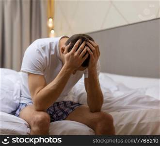 sleep disorder, insomnia and mental health problems concept - unhappy man sitting on bed at night. unhappy man sitting on bed at night