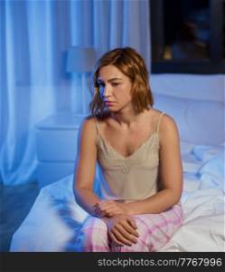 sleep disorder, insomnia and mental health problems concept - unhappy woman in pajamas sitting on bed at night. unhappy woman in pajamas sitting on bed at night