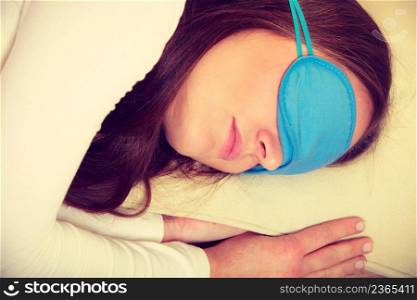 Sleep equipment concept. Portrait of brunette woman sleeping in blue eye mask. Studio shot on beige background. Brunette woman sleeping in blue eye sleep mask