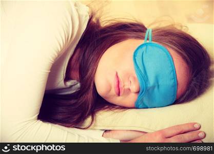 Sleep equipment concept. Portrait of brunette woman sleeping in blue eye mask. Studio shot on beige background. Brunette woman sleeping in blue eye sleep mask